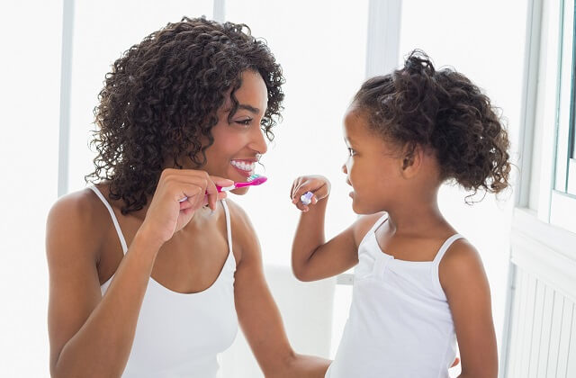 Teeth cleaning represented by a mother and daughter cleaning their teeth.